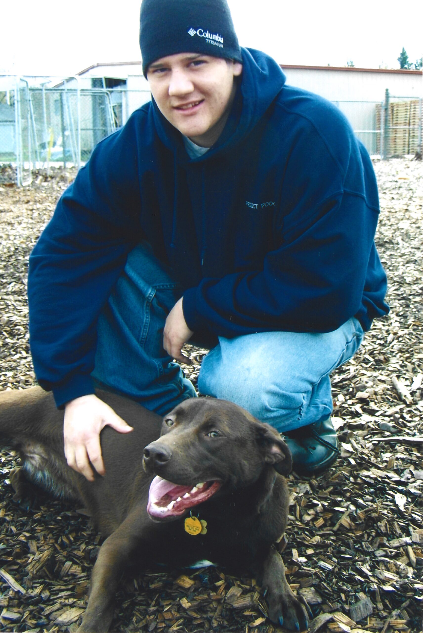 A boy kneeling down and petting a happy brown dog.