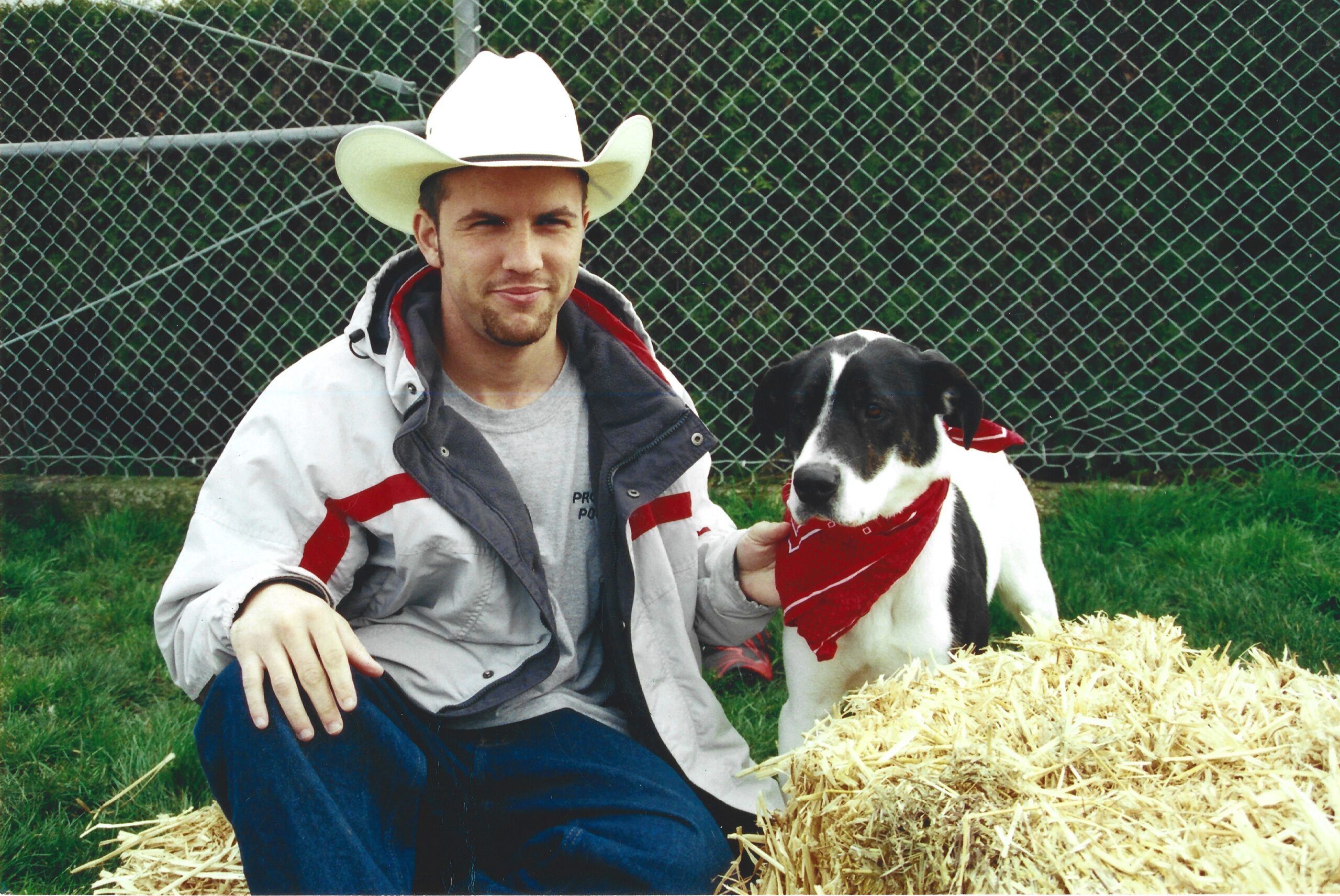 Boy with cowboy boy hat on posing for picture with their dog on a haybail