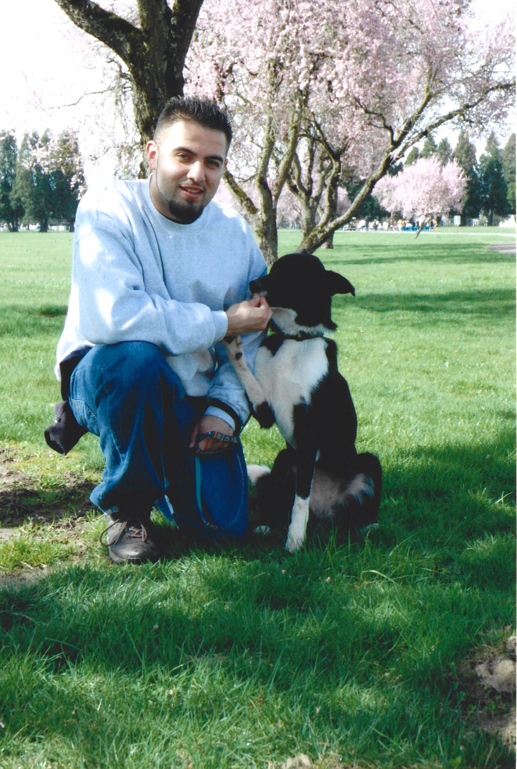 Boy posing for picture with do kneeling in a grassy field giving the dog a treat.