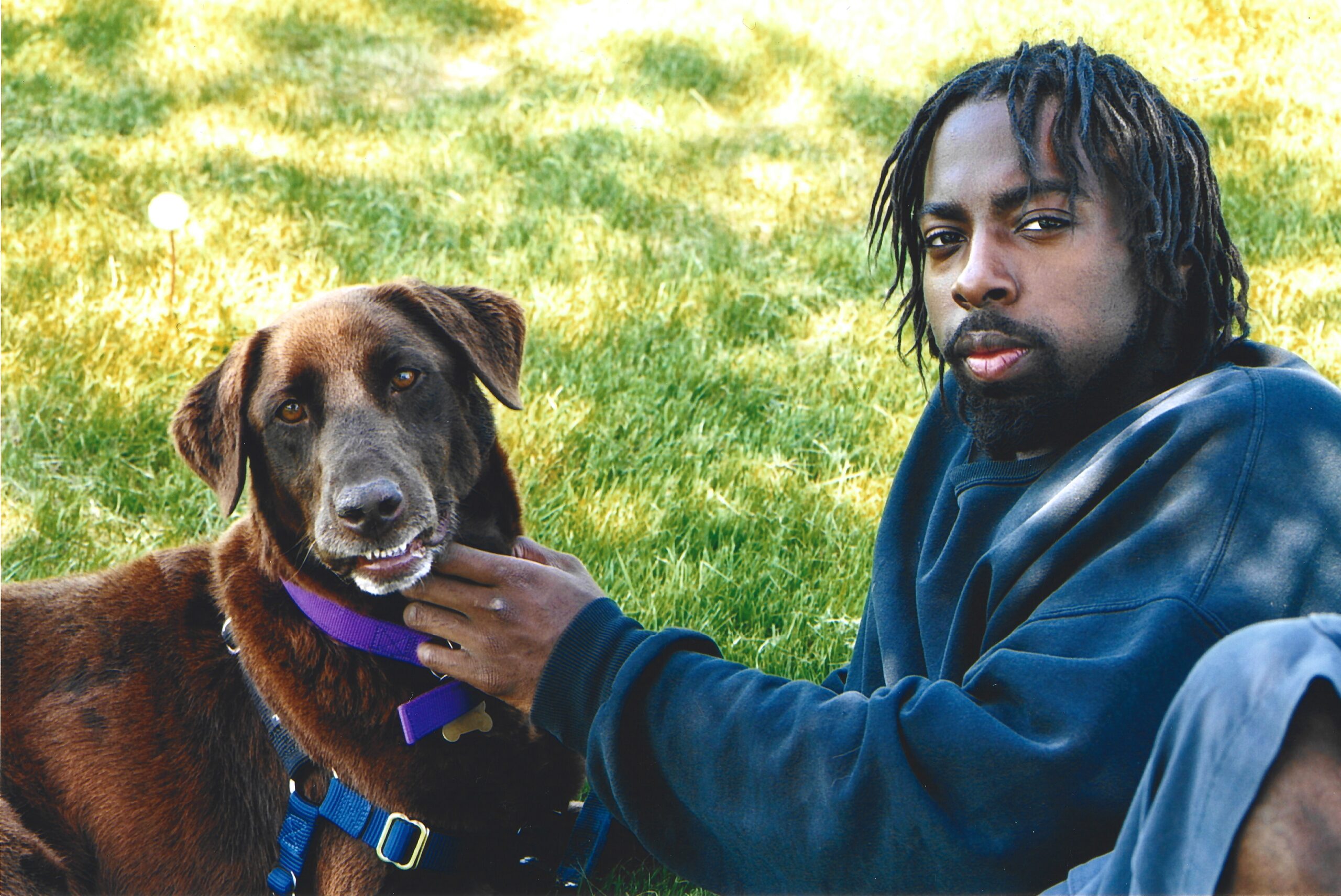 a boy sitting with a brown dog on grass