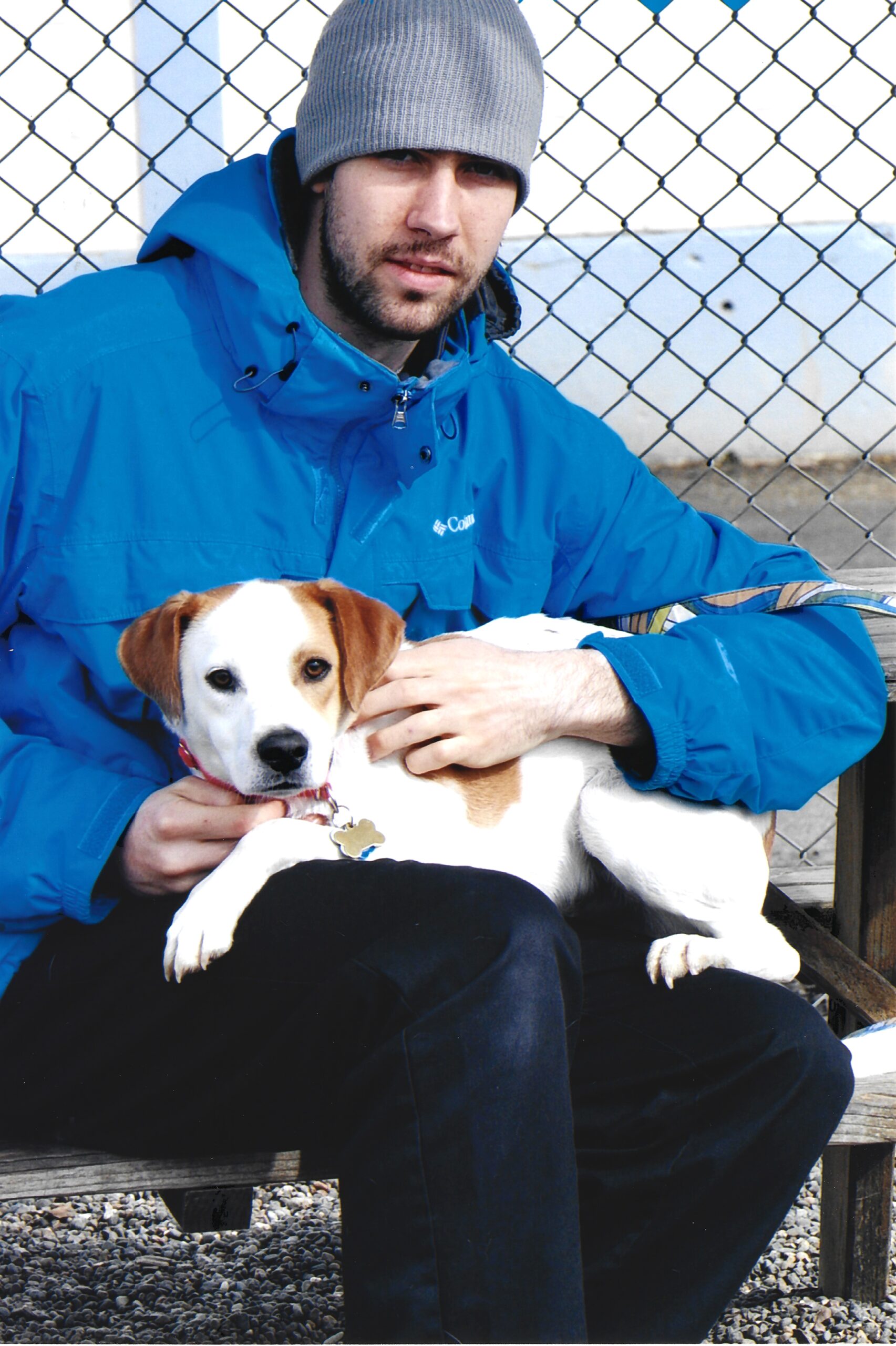 Boy wearing a blue coat sitting on a bench posing for a picture holding a little white dog in his lap.