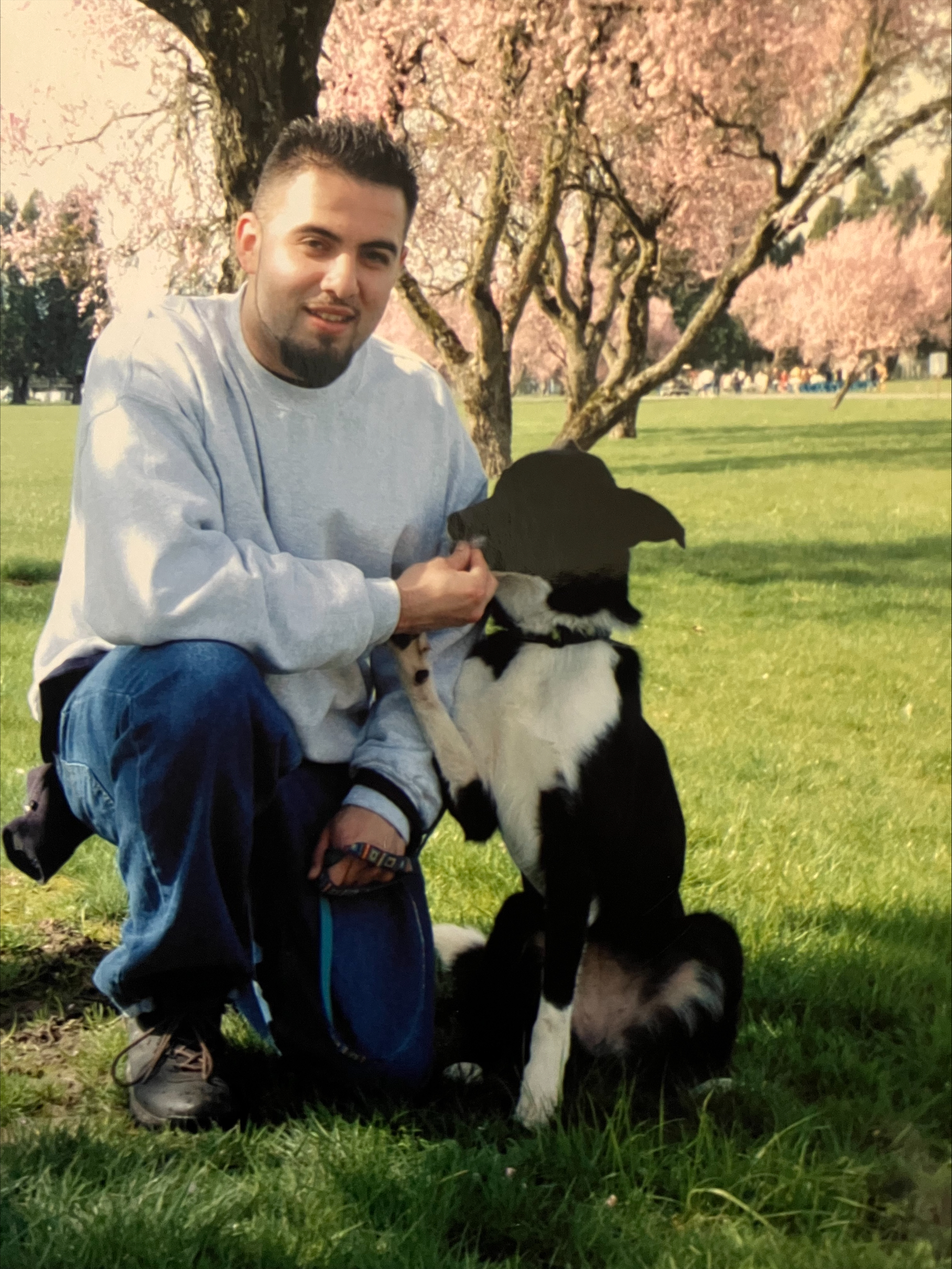 Boy posing for picture with do kneeling in a grassy field giving the dog a treat.